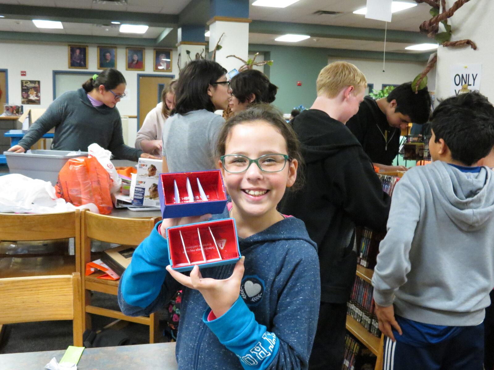 A student beaming while holding up the space-colony model her team built
